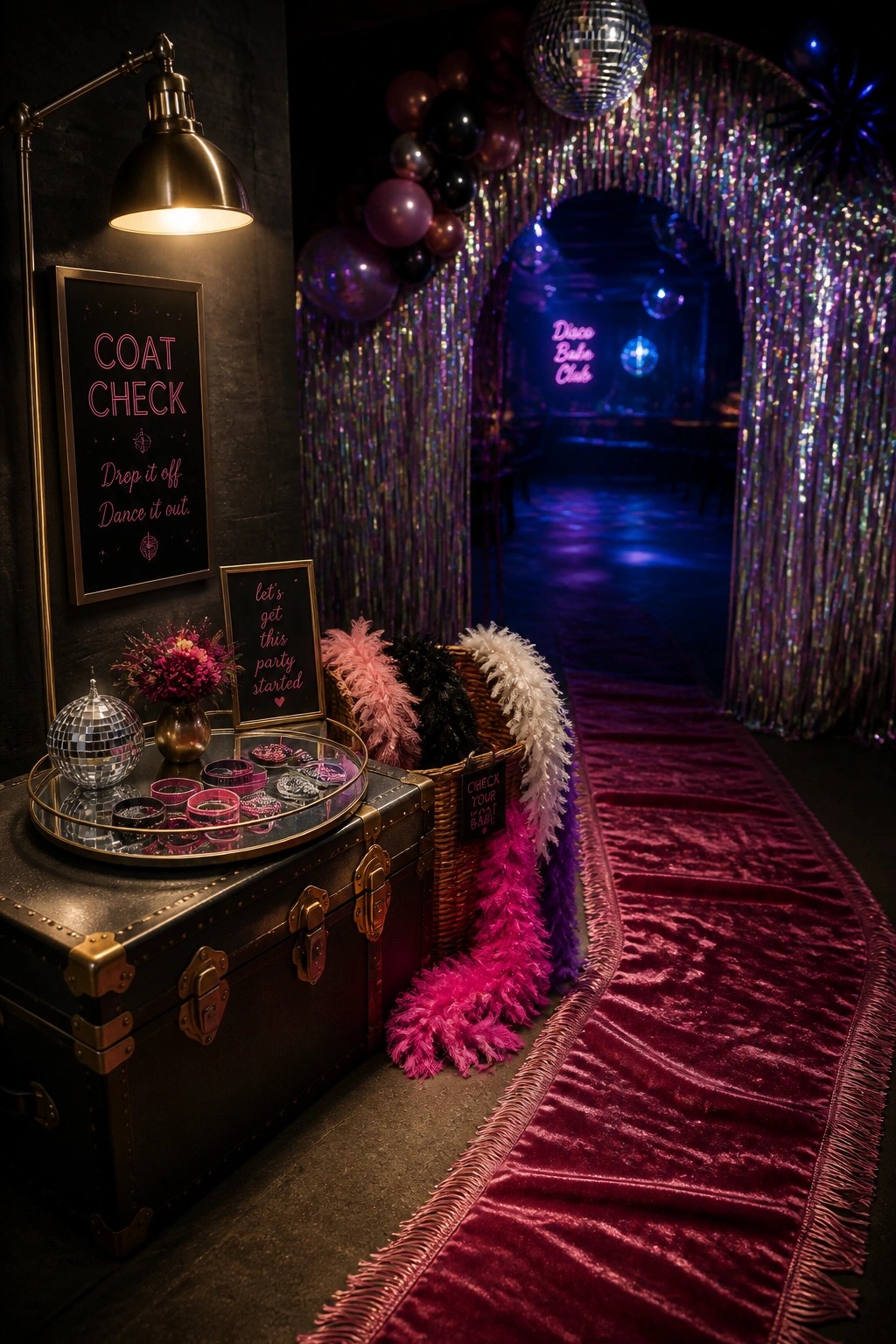 A disco bachelorette party entrance featuring a vintage trunk styled as a coat check station with signs, a tray of accessories, and colorful feather boas beside a red carpet leading to a tinsel archway.